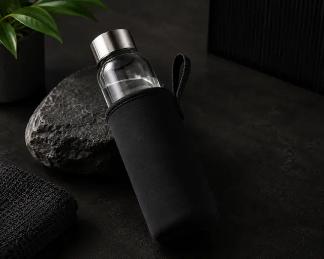 Clear glass water bottle with black sleeve on a dark surface