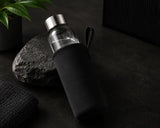 Clear glass water bottle with black sleeve on a dark surface