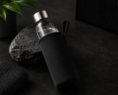 Clear glass water bottle with black sleeve on a dark surface