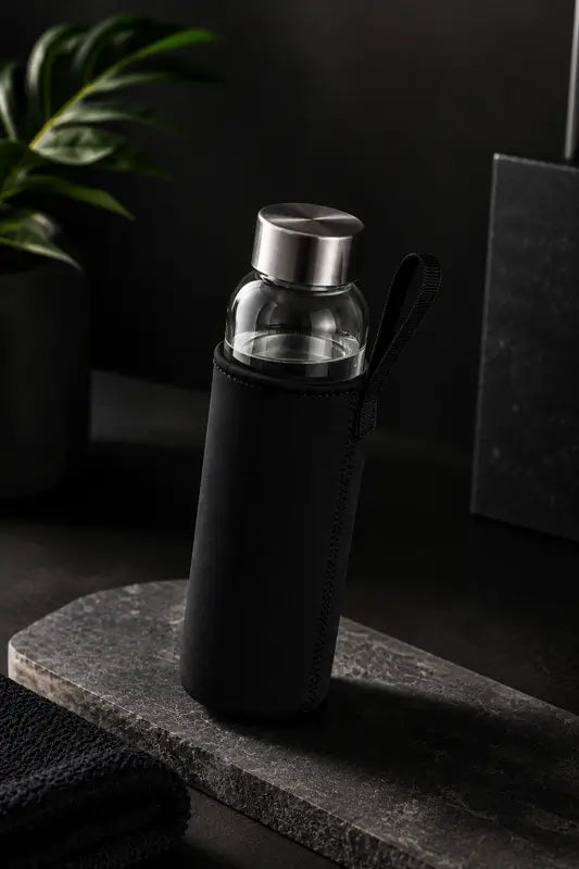 Glass water bottle with black sleeve on a dark surface