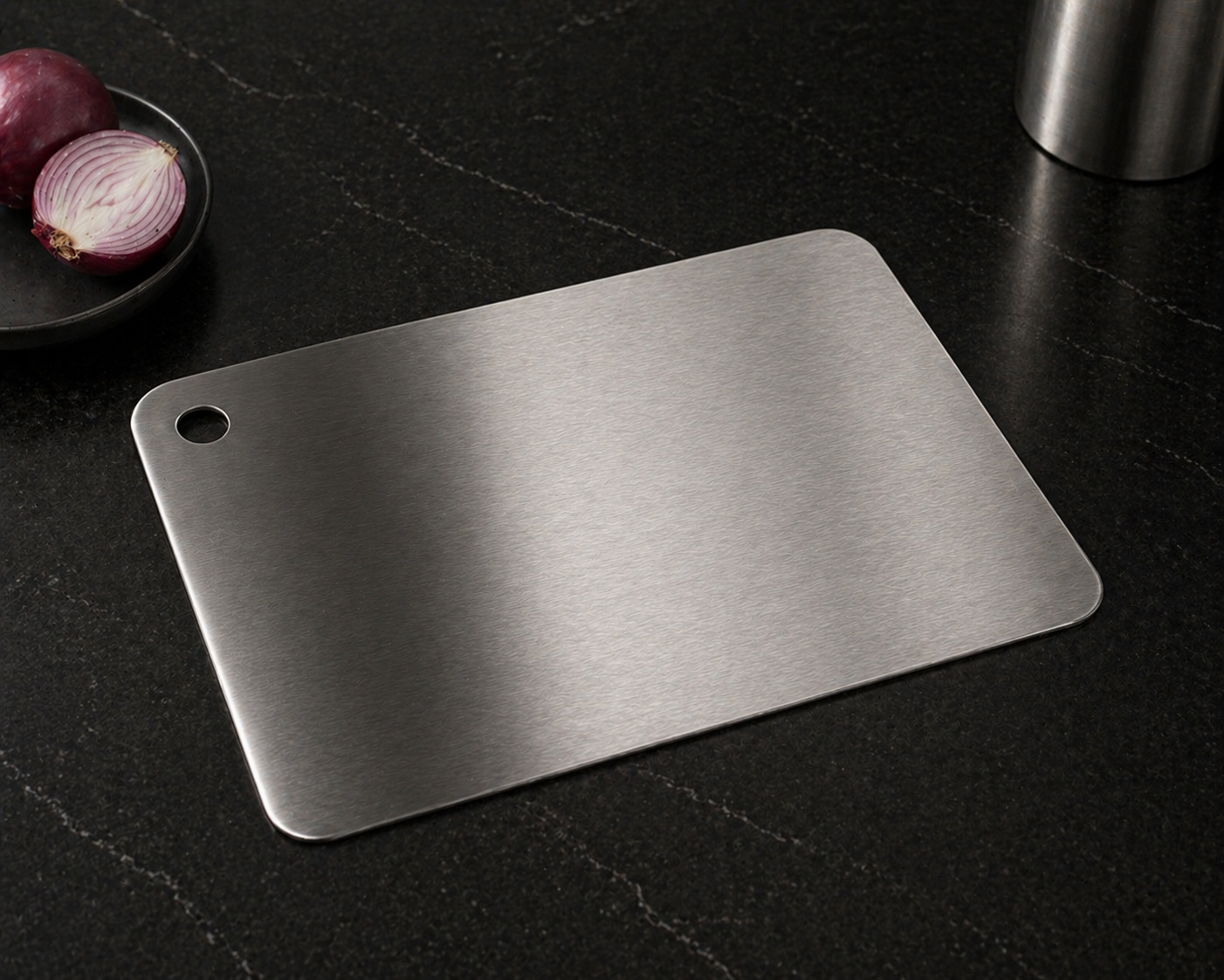 Stainless steel cutting board on a dark surface with red onions in the background