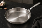 Stainless steel frying pan on a dark kitchen counter with garlic and herbs.